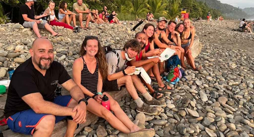 a group of gap year students sit on a rocky beach on an outward bound expedition